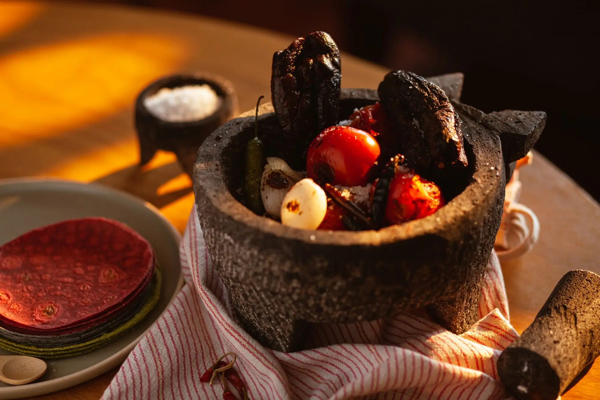 Molcajete con jitomates, chiles y ajos asados junto a tortillas de colores