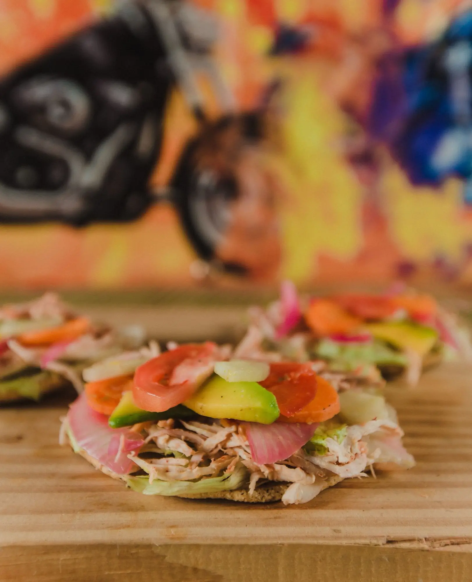 Panuchos con pollo deshebrado, cebolla morada encurtida, aguacate y jitomate sobre tabla de madera